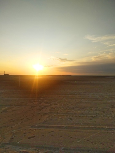 Sie sehen einen schönen Sonnenuntergang über dem weitläufigen Strand von Gravelines. Im Hintergrund blickt man auf den langen Seepier.