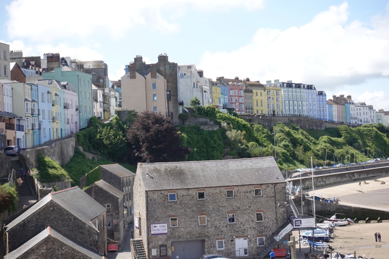 Oberhalb des Hafens von Tenby findet man die pastellfarbenen Häuser, für die Tenby berühmt ist. Die Straße geht entlang der alten Stadtmauer und führt nach oben in die Altstadt. Im Moment ist Ebbe und die Schiffe liegen auf dem Trockenen.