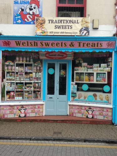 Ein kleines Süßigkeitengeschäft in der Altstadt von Tenby. Die Fassade ist petrol und rosa und im Schaufenster sieht man die großen Gläser mit verschiedenen Bonbonsorten, wie man sie früher auch von deutschen Trinkhallen kennt.