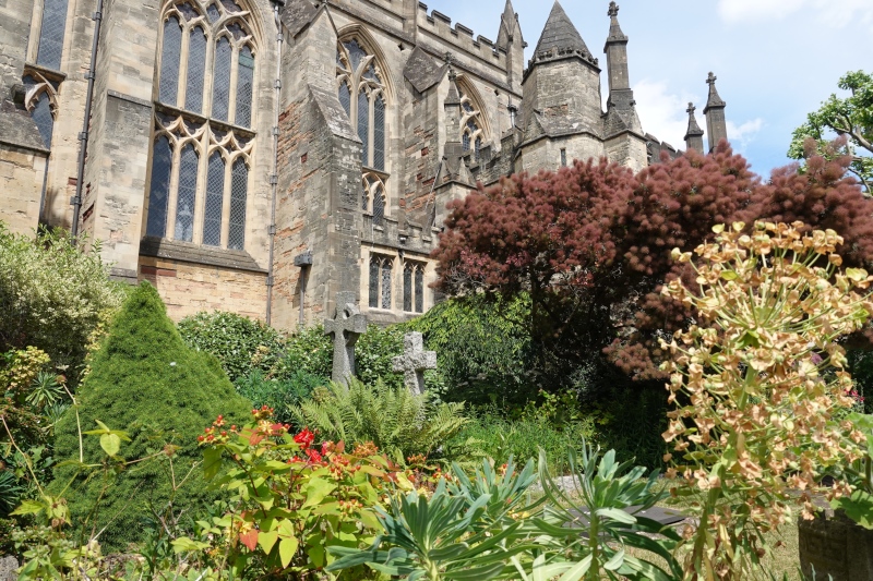 Der Klostergarten der altehrwürdigen Kathedrale von Bristol. Bunte Blumen und Büsche bieten einen schönen Kontrast zum grauen, verwitterten Stein der Kirche.